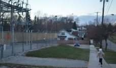 A young child running down a street in Flint, MI, past an electric transformer station