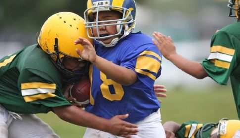 A young boy in a football uniform getting tackled by a boy from the opposing team