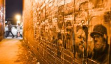 Night shot of alley with photos of people's faces wheatpasted on the bricks