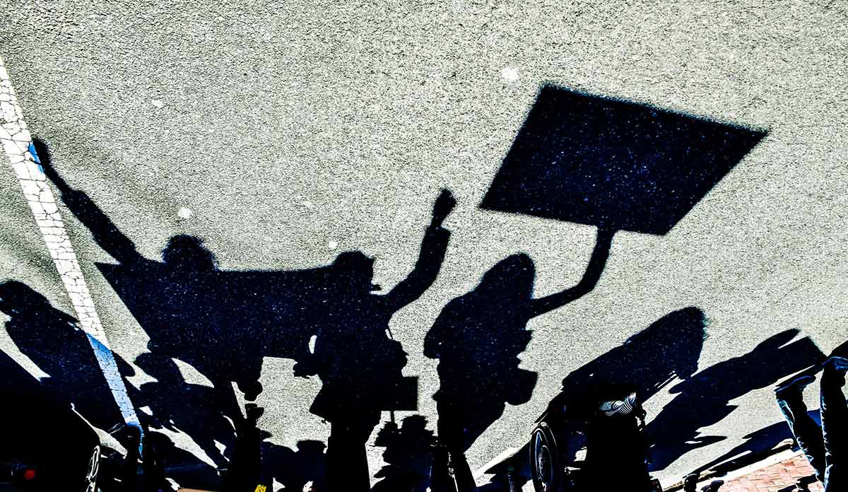 Shadows on the pavement of protesters holding signs