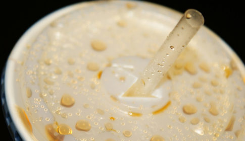 Closeup of the top of a cup of soda with a plastic top and straw