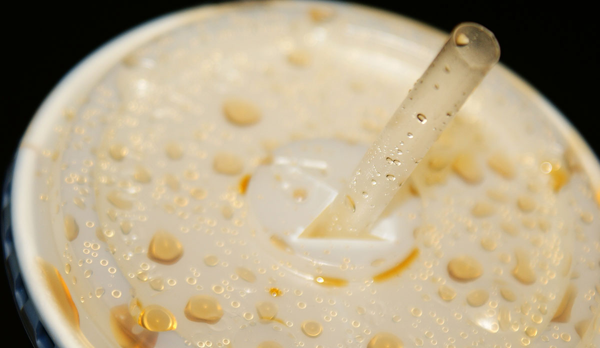 Closeup of the top of a cup of soda with a plastic top and straw