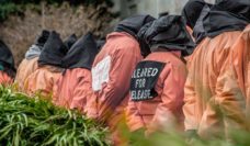 Figures in orange jumpsuits with black hoods