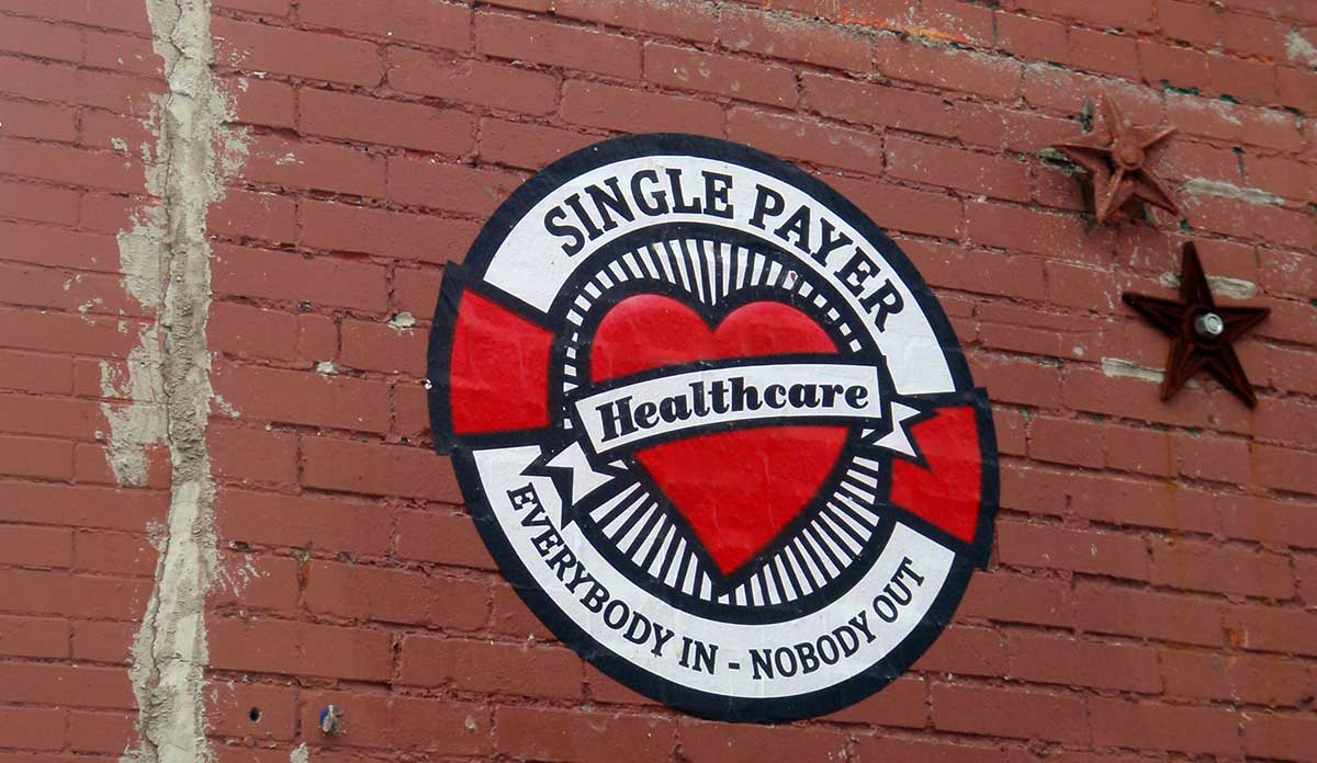 Painted stencil on a brick wall that says Single Payer Healthcare, everybody in, nobody out