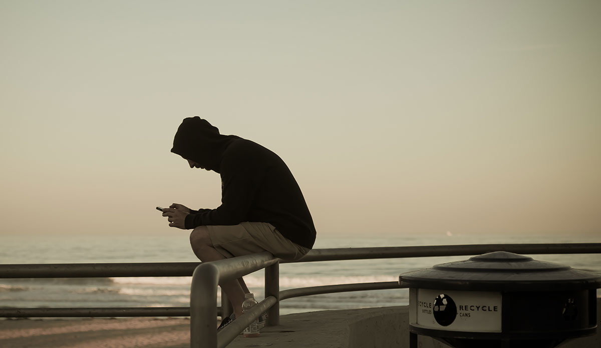 Teenager in a hoodie sitting on a fence looking at a cellphone