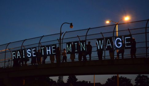 Letters spelling out Raise the Min Wage lit up on a highway overpass