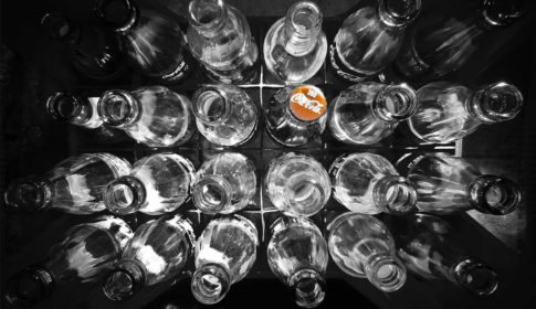 A case of glass soda bottles, one with a red Coca-Cola cap