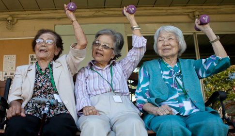 Three older women lifting weights above their heads and smiling