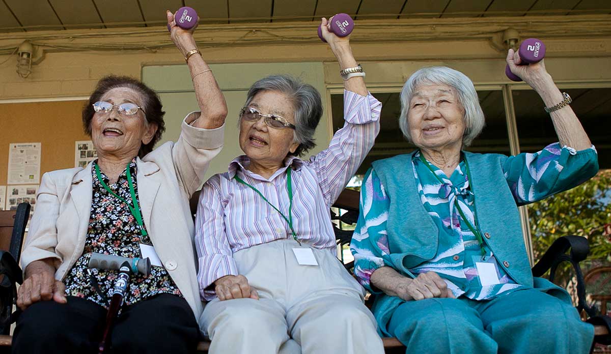 Three older women lifting weights above their heads and smiling