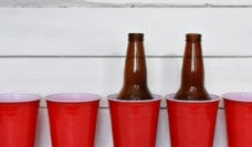A row of red solo cups and two beer bottles