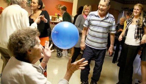 Dance at a nursing home with an older woman reaching for a blue balloon