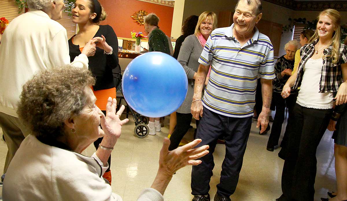 Dance at a nursing home with an older woman reaching for a blue balloon