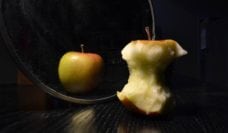 An apple core in front of a mirror showing a full apple