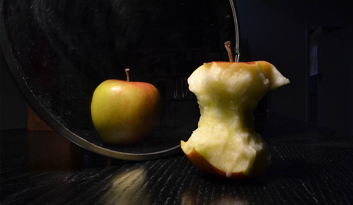 An apple core in front of a mirror showing a full apple
