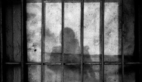 Black and white photo of bars with a person's silhouette behind them