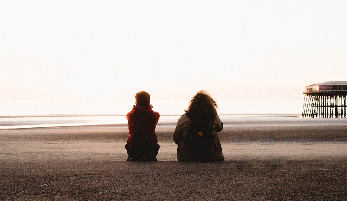 Two young people sitting side by side looking out at the ocean
