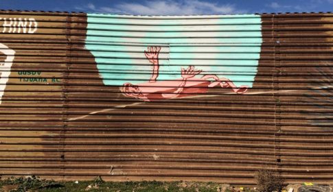 Mural painted on border wall of a gap with a person lying on their back, reaching toward blue sky