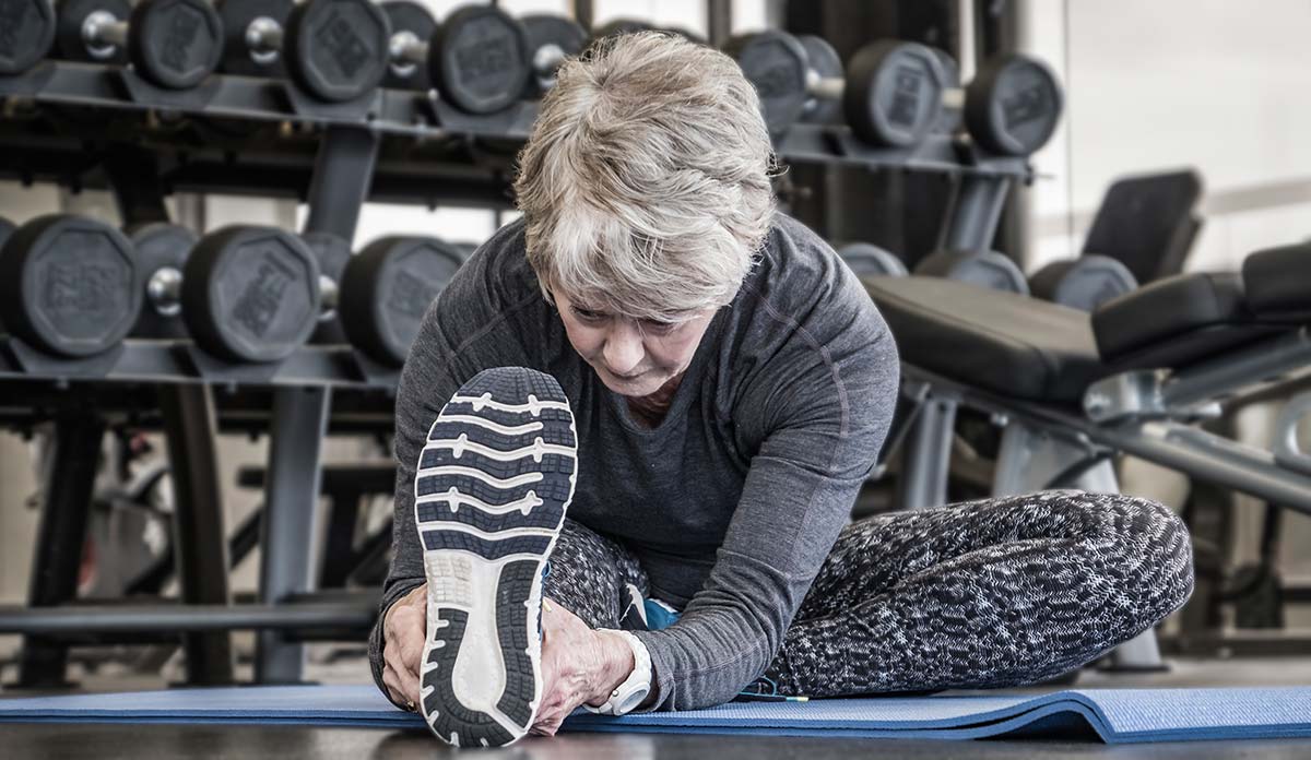 Older woman stretching her leg on a mat a the gym