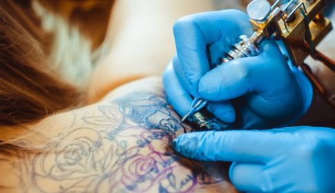 Hand with tattoo needle working on a flower tattoo