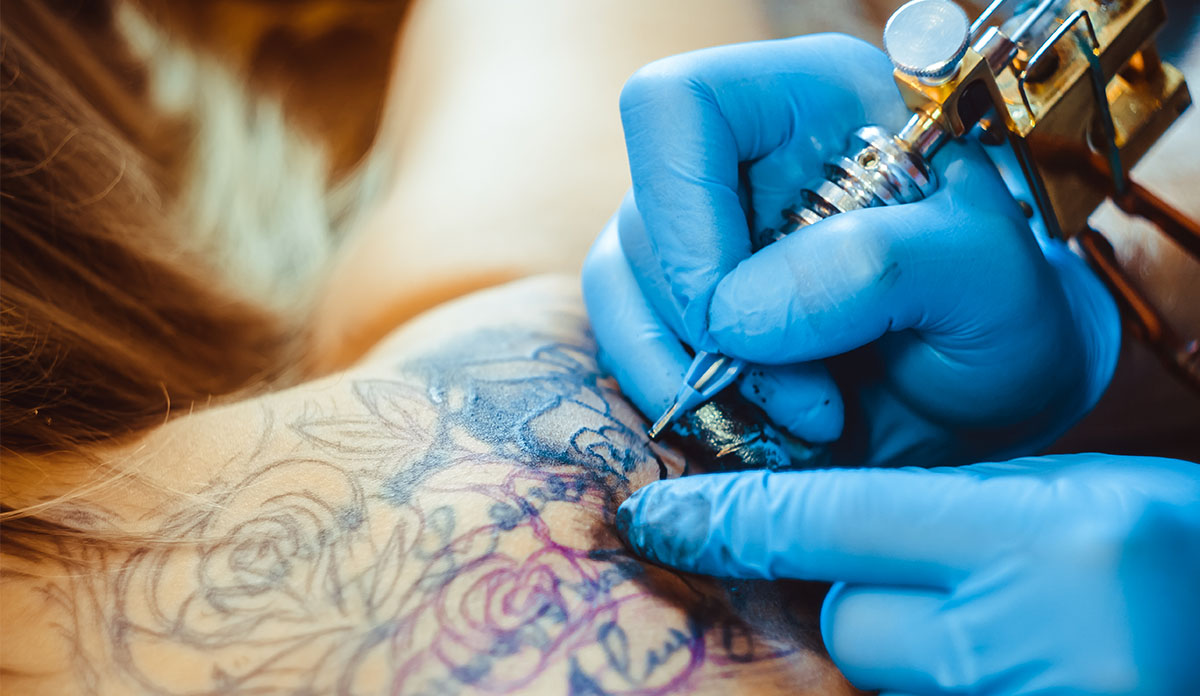 Hand with tattoo needle working on a flower tattoo