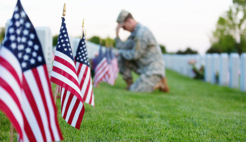 soldier kneeling in cemetery with American flags.
