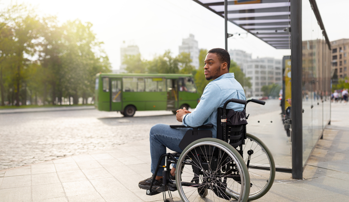 man in wheelchair waits at bus stop for accessible public transportation