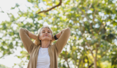 Elderly woman relaxing and breathing fresh air with sunlight in outdoors park