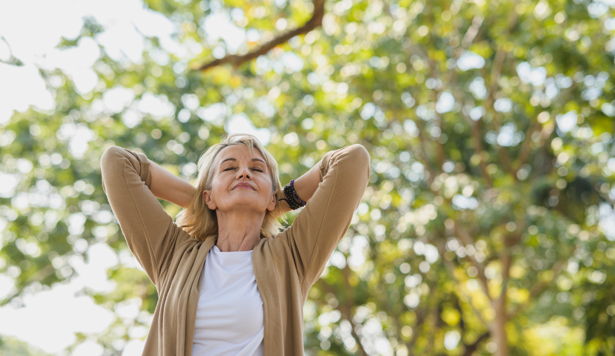 Elderly woman relaxing and breathing fresh air with sunlight in outdoors park