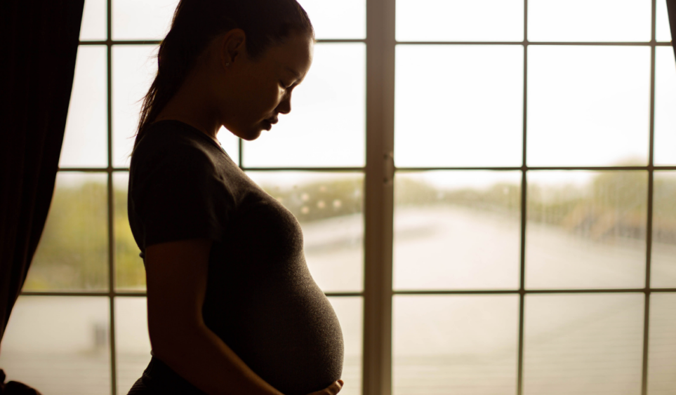 woman in front of window looks down at pregnant belly