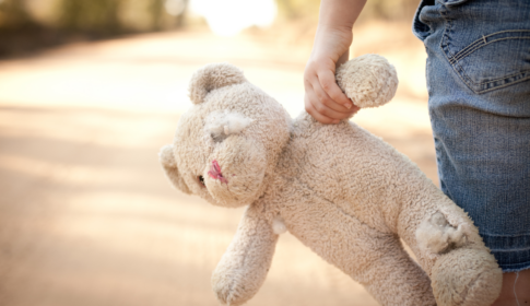 child holding old, tore up teddy bear