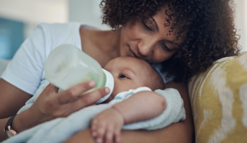 mother feeding newborn child with a bottle on the couch