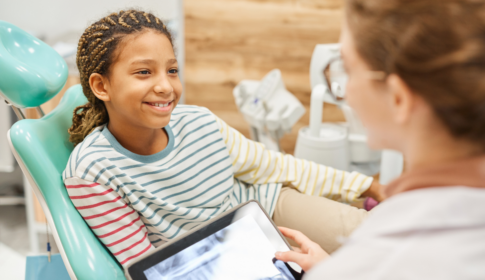 young girl sitting in chair, speaking with the dentist about her teeth