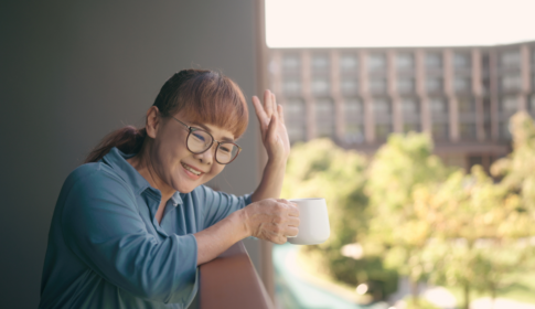 older asian woman smiling and waving to her neighbor below