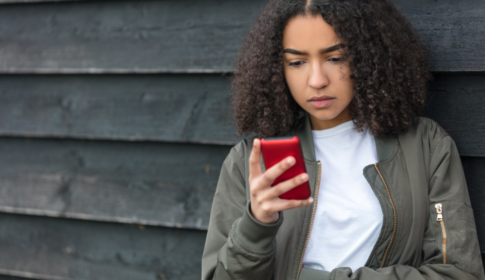 young girl looks at phone with depressed face