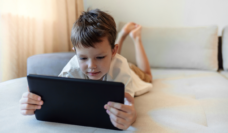 young boy laying on couch watching YouTube on iPad