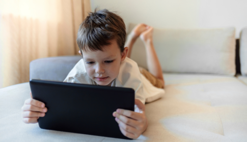 young boy laying on couch watching YouTube on iPad