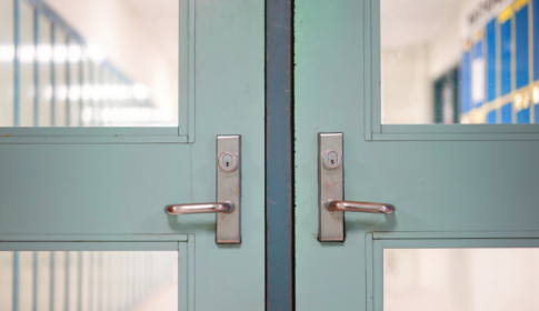 Selective focus on closed door and handles with blurred hallway, locker background. School safety concept