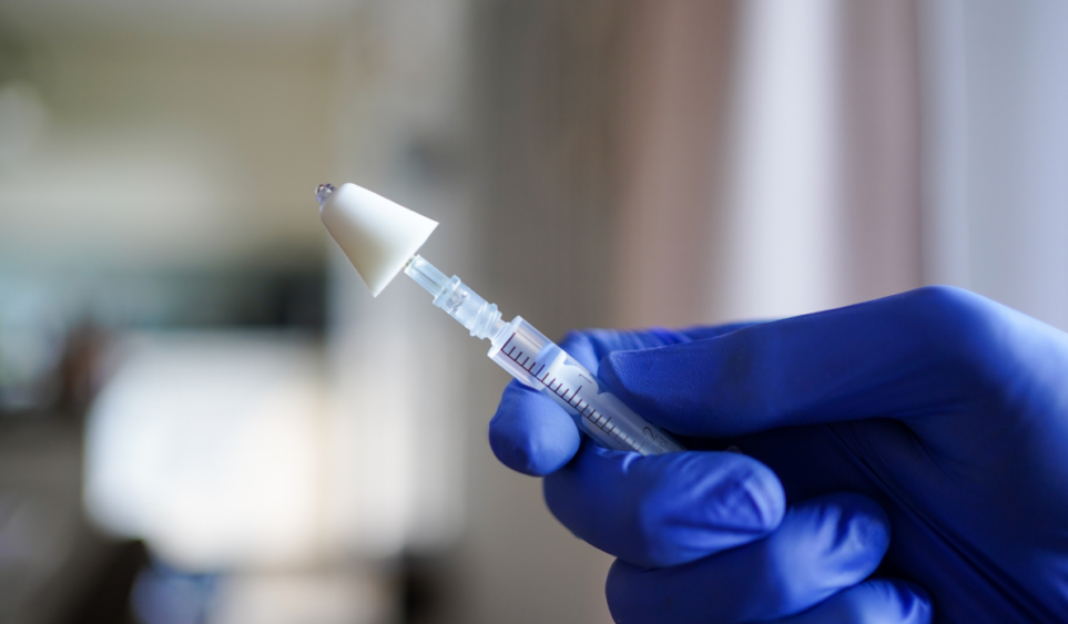 Hand holding a syringe with a mucosal atomization decive (MAD) used for intranasal application of drugs, like naloxone, a drug used for opioid overdose prevention